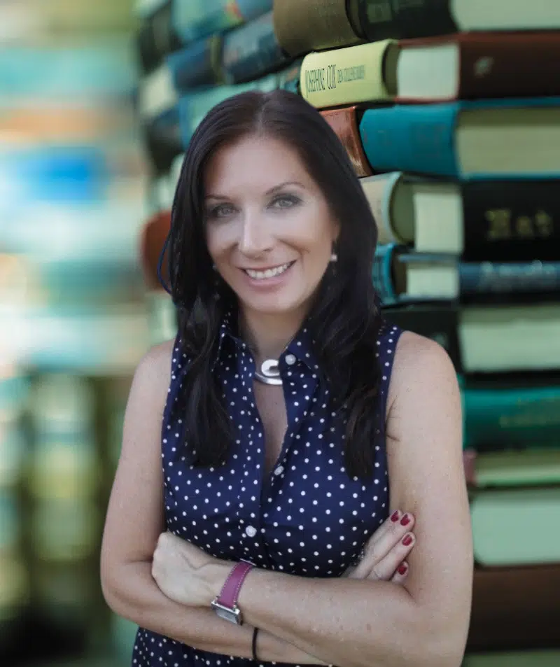 Renee Blodgett, founder of Blue Soul Media, standing in front of a stack of books